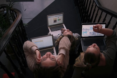 三人坐在梯子上使用笔记本电脑